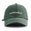 A dark olive green baseball cap embroidered with the word overstimulated on the front.