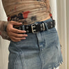 A close-up of a woman wearing a black leather belt with silver studs over a denim skirt.