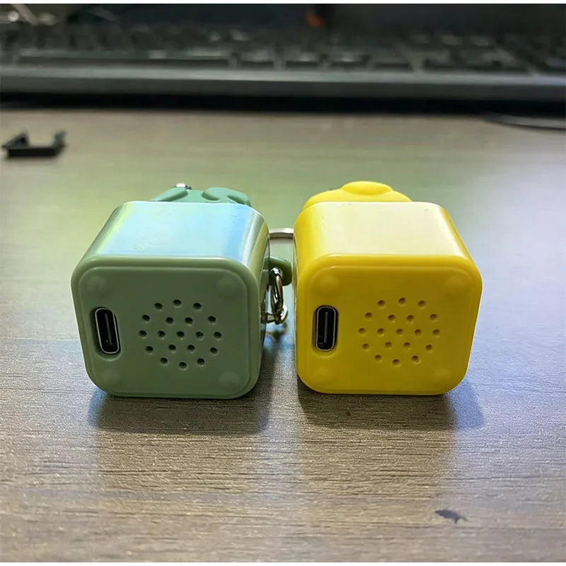Two fidget frog keychains, one green and one yellow, resting on a wooden desk surface.
