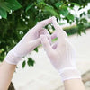 A pair of sheer lace fishnet evening gloves are shown against a blurred green outdoor background.