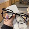 A person is holding a pair of black anti-blue light clear framed eyeglasses against a white background.