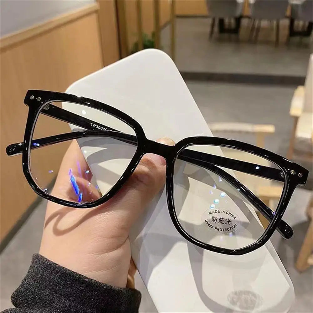 A person is holding a pair of black anti-blue light clear framed eyeglasses against a white background.
