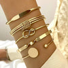 A stack of gold geometric minimalist bracelets worn on a wrist against a light background.