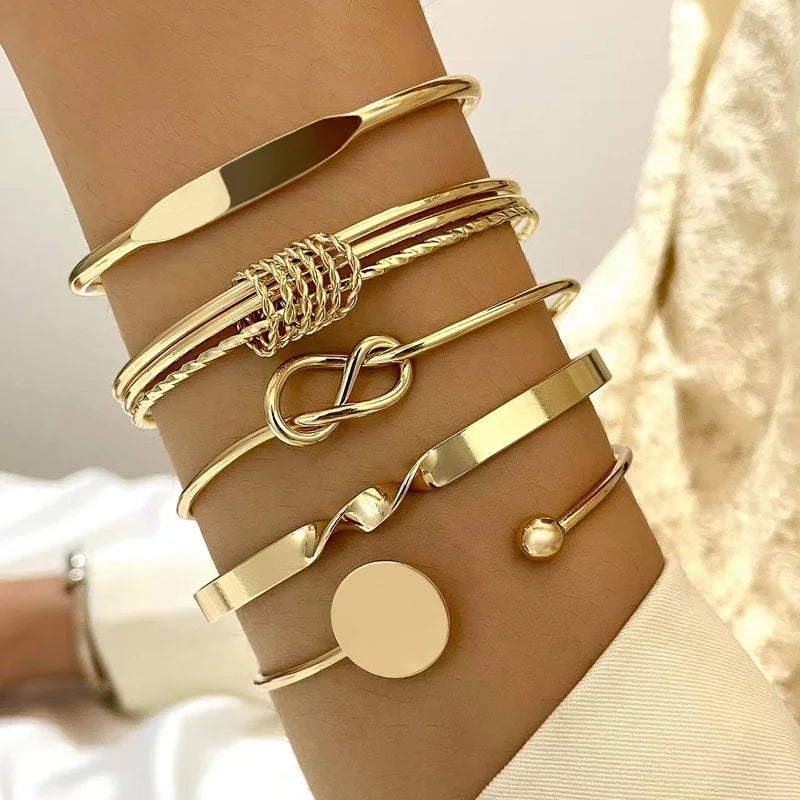 A stack of gold geometric minimalist bracelets worn on a wrist against a light background.