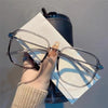A pair of clear framed retro anti-blue light sunglasses resting on a white paper next to a dark blue cylindrical object.