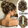 A woman shows off a voluminous curly messy bun hairstyle with blonde and brown highlights.