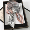 A luxury silk scarf featuring an intricate paisley pattern in pink and black tones, displayed in a dark frame.