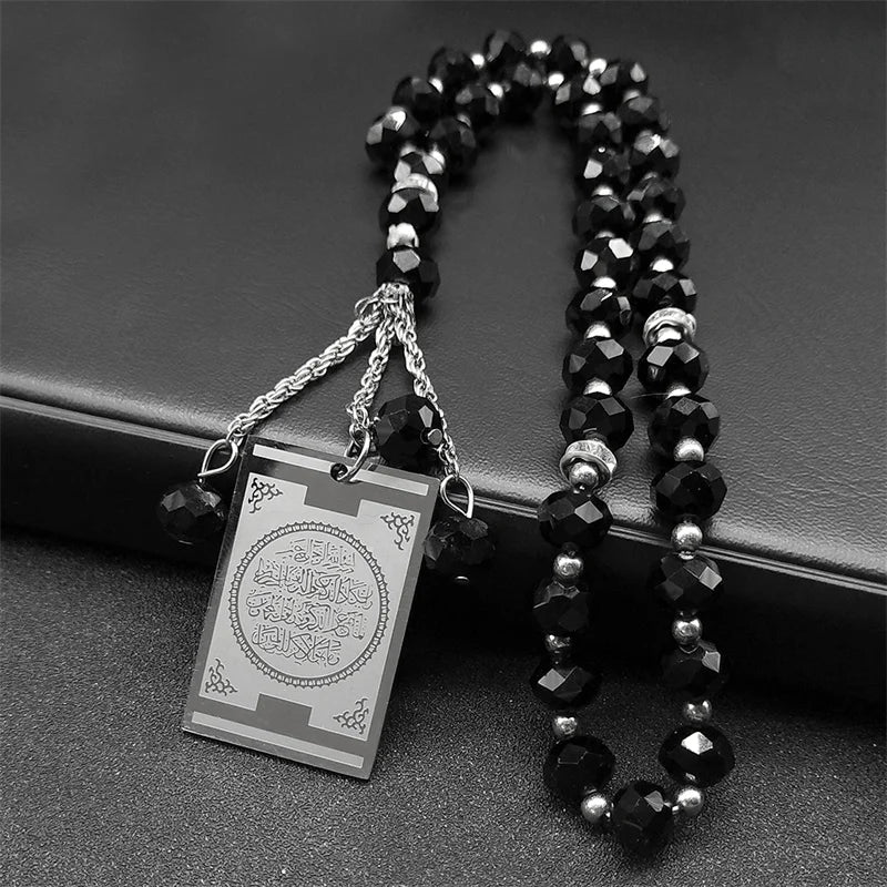 A black beaded necklace with a stainless steel Quran Arabic car pendant on a dark background.