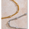A close-up of a gold-toned charm necklace and a silver-toned chain necklace displayed on a light pink marble surface.