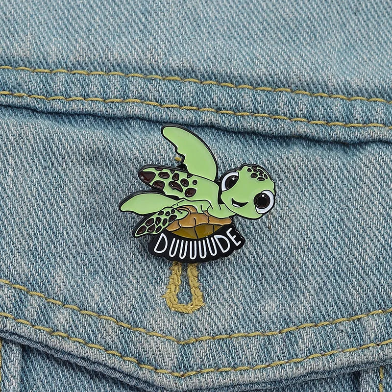 A green sea turtle enamel lapel pin brooch is pinned onto a blue denim fabric.