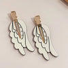 A pair of gold-toned angel wing hair clips with a white, cutout design and small rhinestones.