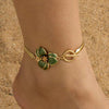 Gold-toned flower pendant anklet with a green enamel bloom worn on a person's ankle.