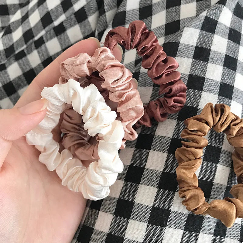 A hand holds several elegant simulation silk hair ties in shades of dusty rose, beige, and brown against a black and white ch