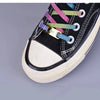 A close-up of a black canvas shoe with multicolored embroidery and gold charms on the laces.