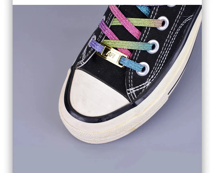 A close-up of a black canvas shoe with multicolored embroidery and gold charms on the laces.