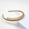 A close-up of a tan, braided hair headband with small teeth, resting on a white surface.