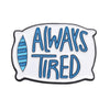 An enamel pin featuring the text ALWAYS TIRED in blue lettering with a striped design.