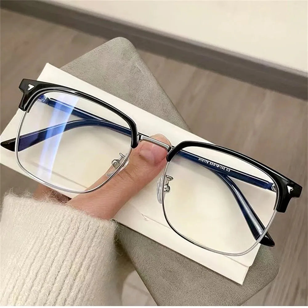 A pair of clear anti-blue light eyeglasses resting on a white card next to a person's hand.