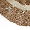 Primer plano de un sombrero Panamá de paja tejido a mano con tiras de tela beige claro y pequeñas borlas decorativas.
