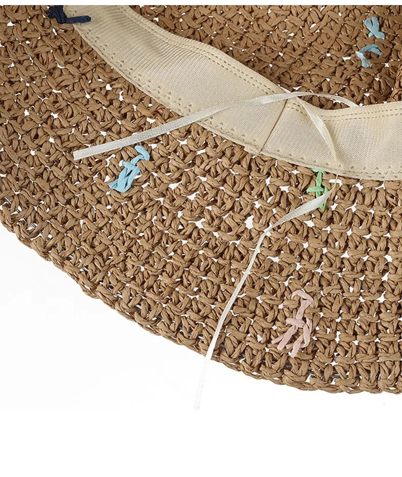 Primer plano de un sombrero Panamá de paja tejido a mano con tiras de tela beige claro y pequeñas borlas decorativas.