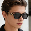 Nahaufnahme eines männlichen Models mit schwarzen retro-eckigen Metall-Sonnenbrillen mit goldenen Akzenten.