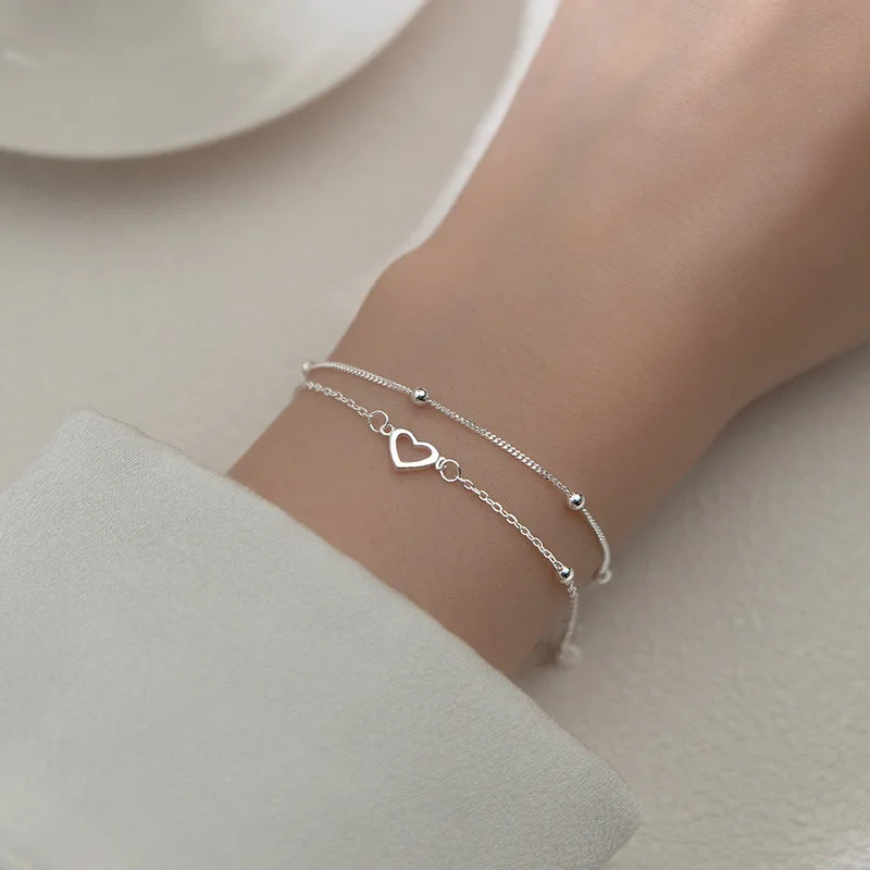 A close-up of a sterling silver double heart charm bracelet worn on a wrist against a light background.