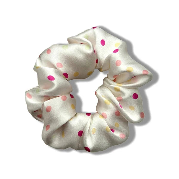 A close-up of luxury pure silk hair scrunchies in a cream color with scattered pink and yellow polka dots.