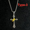A silver crown cross necklace with a yellow enamel detail displayed against a black background.