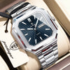 A silver stainless steel watch with a dark blue dial and luminous hands is displayed on a light-colored surface.