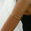 A close-up of a wrist wearing a set of six gold-plated swirl cuff armbands.