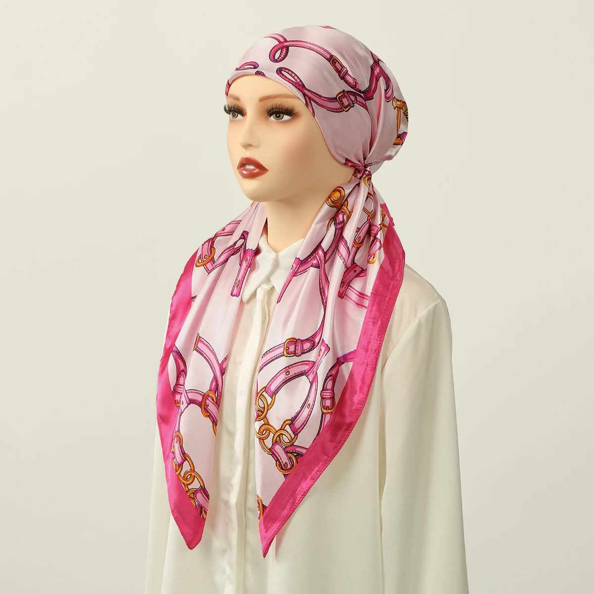 A woman models a pink satin silk hijab headband cap with gold embroidery against a light background.