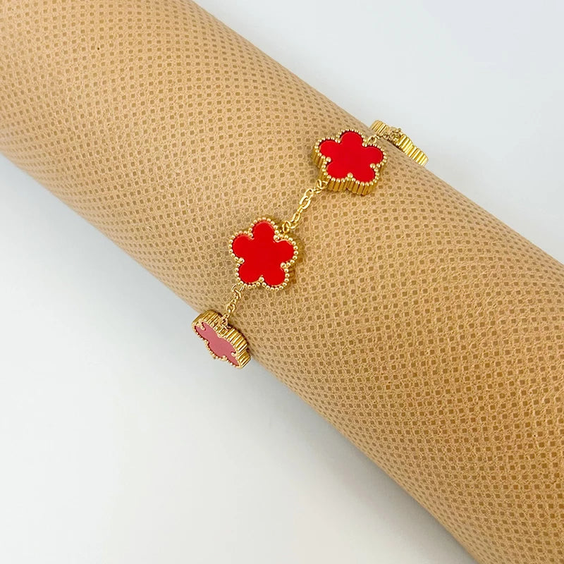 A gold plated stainless steel double-sided petal bracelet with red floral charms is displayed on a rolled beige fabric.