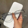 A hand holds a pair of clear retro half gold anti blue light eyeglasses on a white stand.