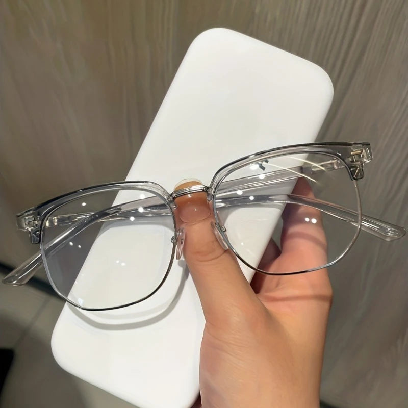 A hand holds a pair of clear retro half gold anti blue light eyeglasses on a white stand.