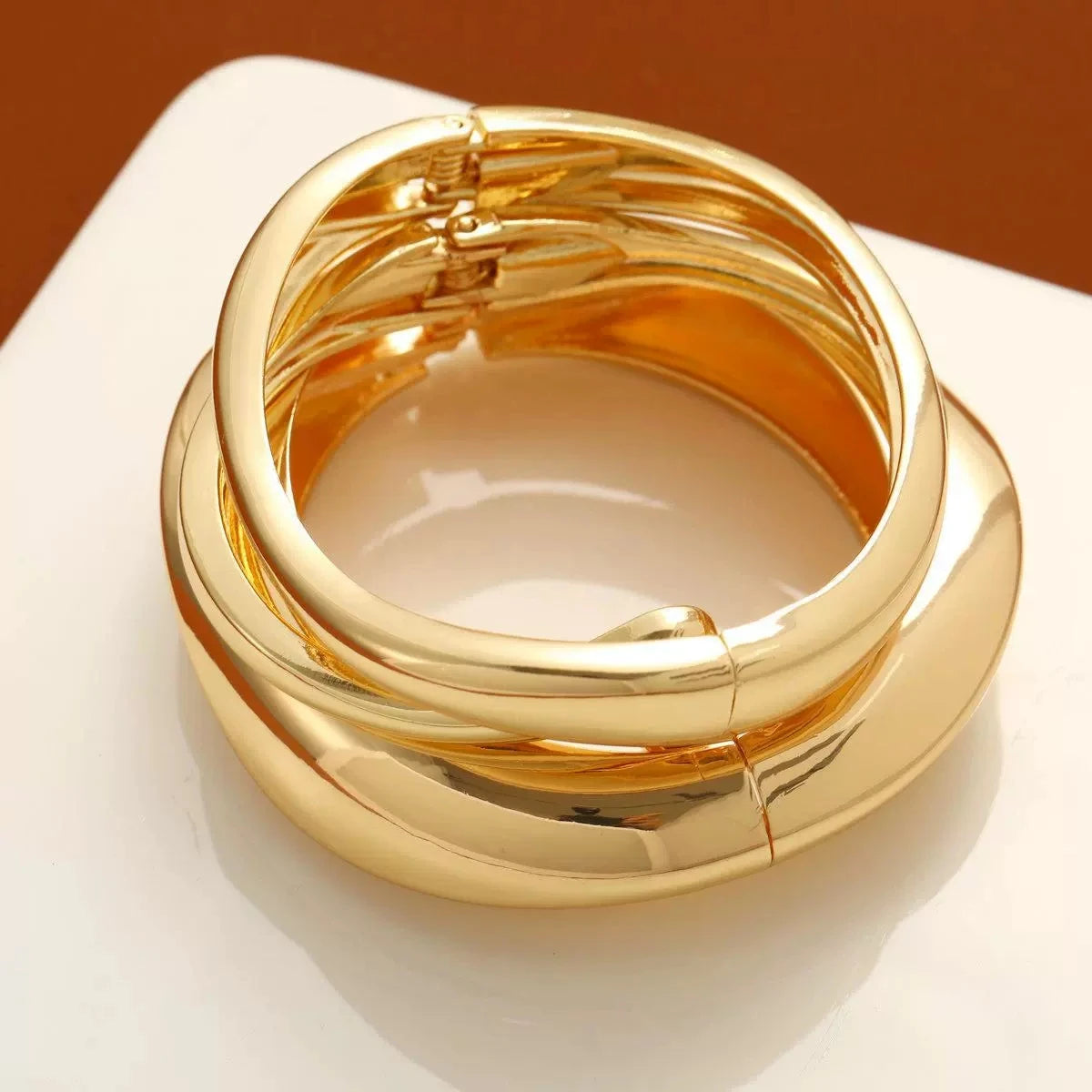 A stack of thick, gold bangle bracelets displayed on a white surface.