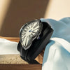 A silver fashion quartz wristwatch with a Roman dial and blue accents rests on a light wooden surface.