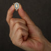 A hand holds a gold-toned centerpiece connector for a rosary, featuring a blue and white enamel design.