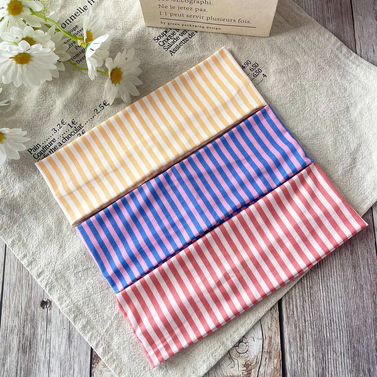 Collection de bandeaux pour cheveux rayés, jaunes, bleus et roses, présentés sur un tissu clair.