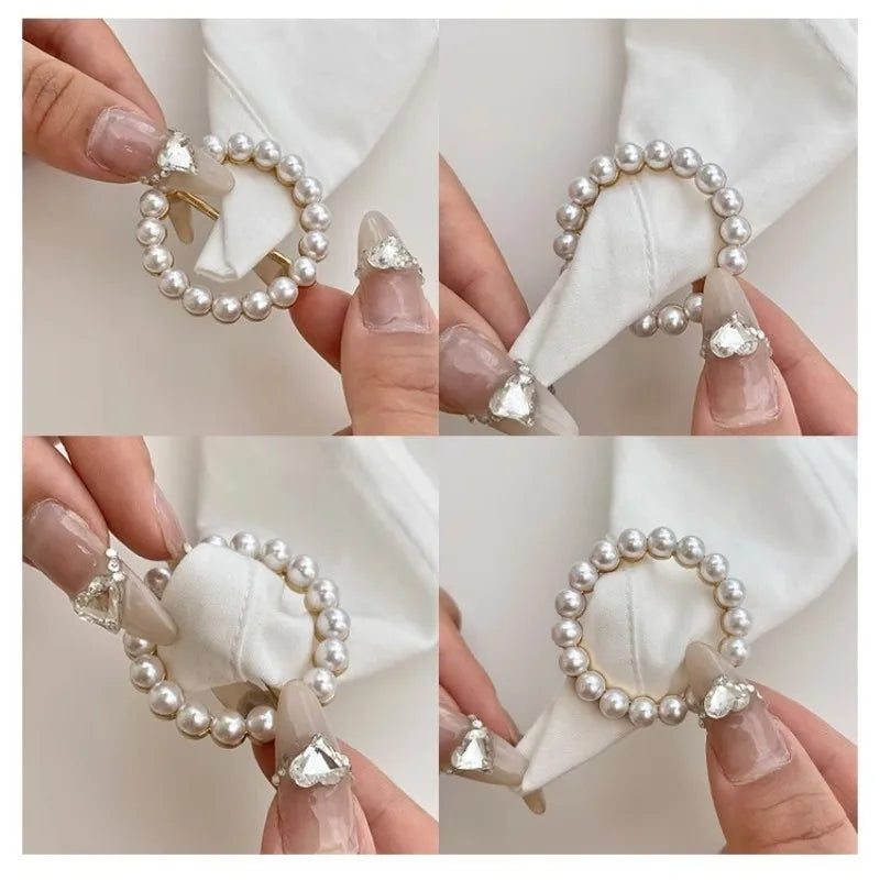 Close-up of elegant pearl and rhinestone decorative button clips being held by fingers against a white fabric background.