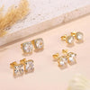 Gold plated simulated diamond stud earrings displayed on a light background next to dried floral elements.