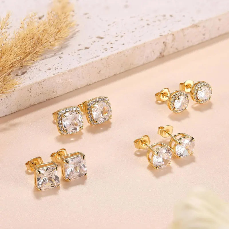 Gold plated simulated diamond stud earrings displayed on a light background next to dried floral elements.