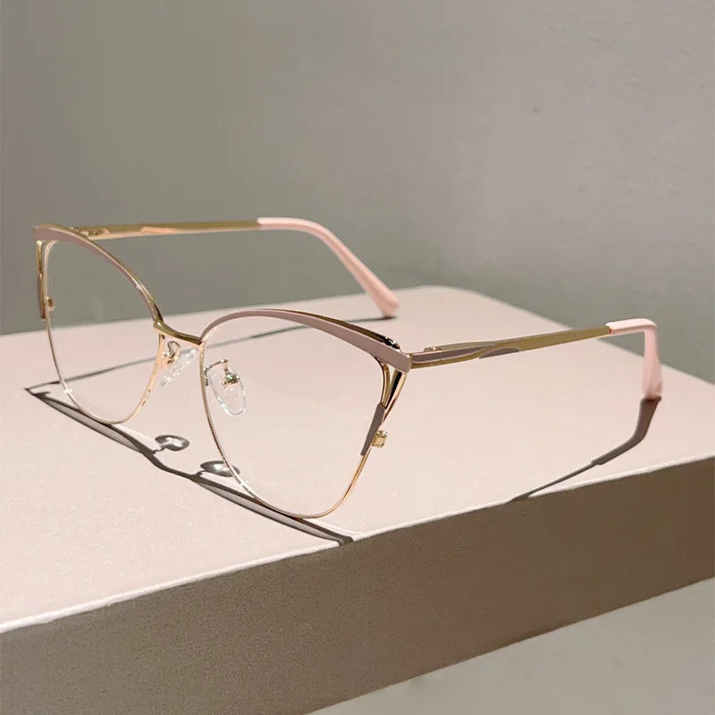 Un par de gafas de computadora metálicas finas, tono dorado con acentos rosados, sobre una superficie blanca.
