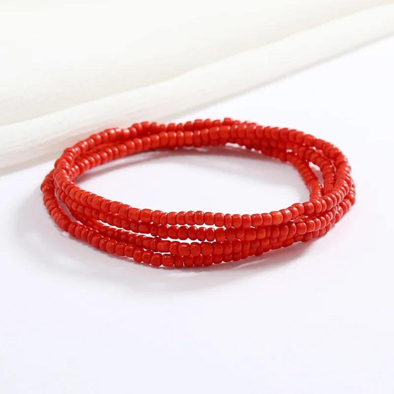Una pila de collares hechos a mano de cuentas rojas brillantes sobre una superficie blanca.