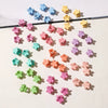 A collection of colorful mini flower hair clips in shades of blue, pink, yellow, and green scattered on a white background.