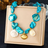 A necklace featuring blue and white sea glass-like pendants shaped like starfish and hearts, presented in a light pink box.