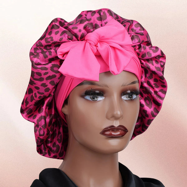 A pink satin sleep bonnet with a leopard print pattern tied in a bow, displayed on a mannequin head.