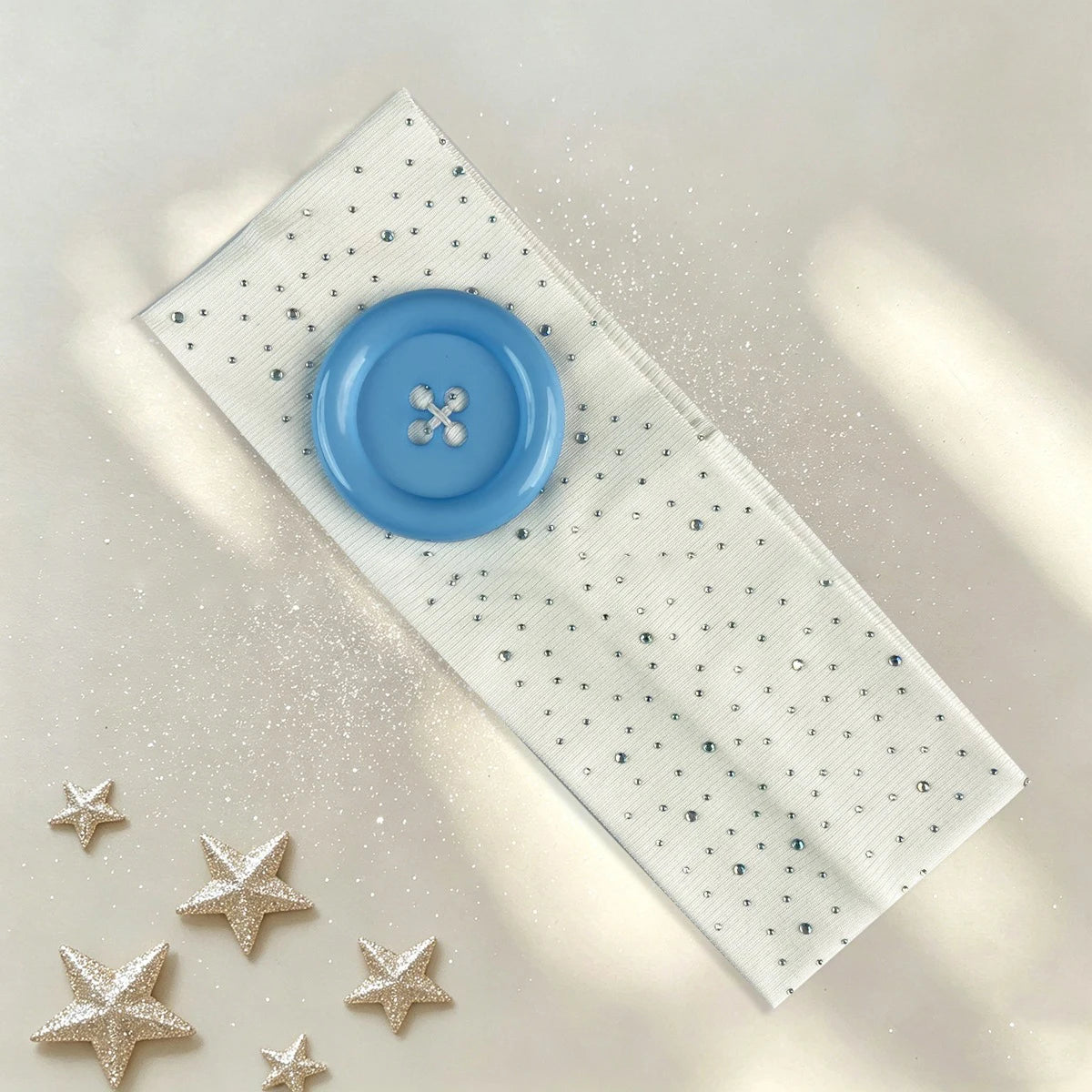 A light blue polka dot button headband with silver accents and glitter stars lying on a pale background.