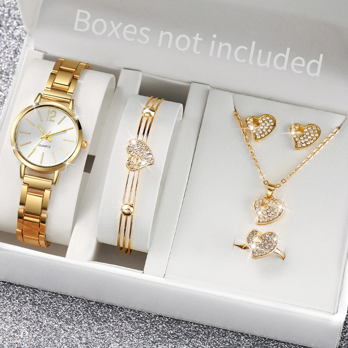 A white box contains a gold-toned quartz watch, a gold bracelet, and a gold necklace with heart pendants.