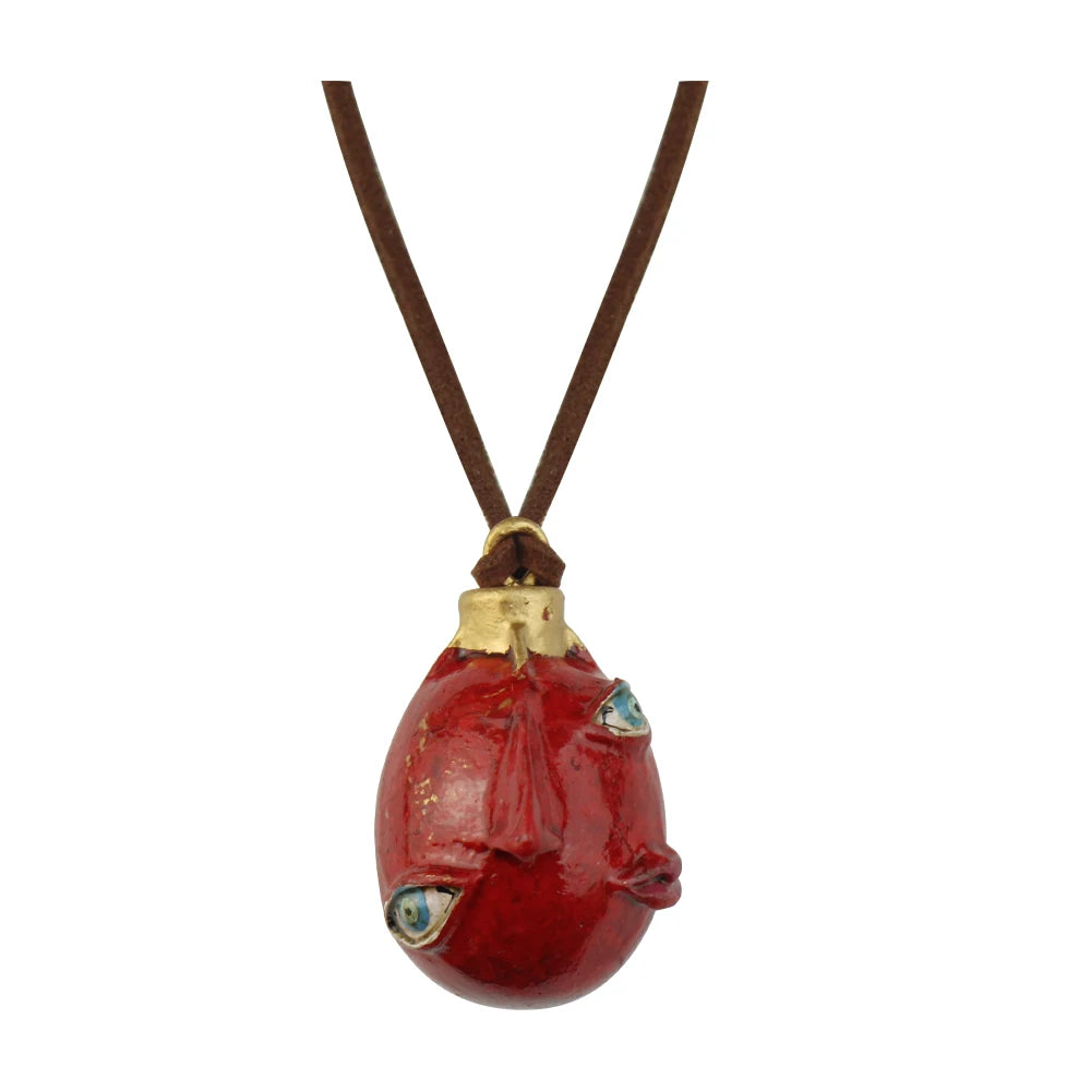 Collar con dije de rostro estilizado rojo, cierre dorado y cordón marrón.