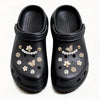 Un par de charm para zapatos negros con diseños florales y de mariposa de diamantes dorados y blancos.